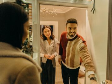 A couple greeting a guest at their doorway, capturing the warmth of a home during the holiday season.