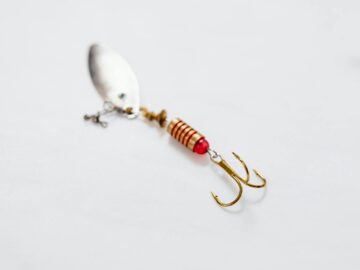 Detailed view of a metallic fishing lure with a sharp treble hook on white surface.