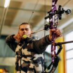 A man intensely focuses on aiming a purple compound bow at an indoor archery range.