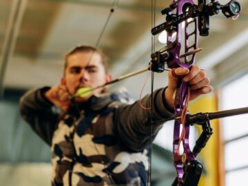 A man intensely focuses on aiming a purple compound bow at an indoor archery range.