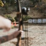 An archer aims at targets at an outdoor archery range, featuring a natural backdrop.