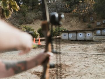 An archer aims at targets at an outdoor archery range, featuring a natural backdrop.