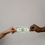 A dollar bill is exchanged between two diverse hands on a neutral background.