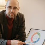 Bald man in red sweater presenting business data with a graph in an office setting.