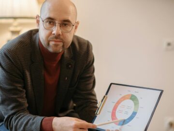 Bald man in red sweater presenting business data with a graph in an office setting.