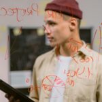 Man strategizing ideas on a glass panel with red marker writings, creating an innovative brainstorming session.