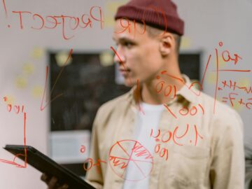 Man strategizing ideas on a glass panel with red marker writings, creating an innovative brainstorming session.