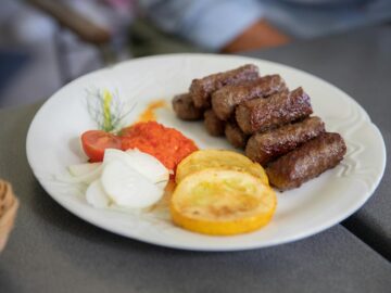 Plate of flavorful grilled cevapi with fresh vegetables and red pepper sauce. Perfect traditional Balkan meal.