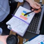 Man working with notes and laptop over a coffee break, analyzing charts.