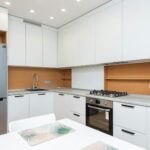Contemporary kitchen with gas stove and oven against table with placemats and refrigerator reflecting shiny lamps in house