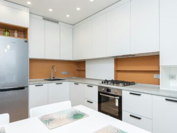 Contemporary kitchen with gas stove and oven against table with placemats and refrigerator reflecting shiny lamps in house