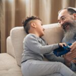 A joyful grandfather and grandson sharing a playful moment on the couch, indoors.