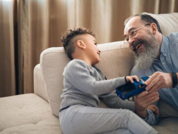 A joyful grandfather and grandson sharing a playful moment on the couch, indoors.