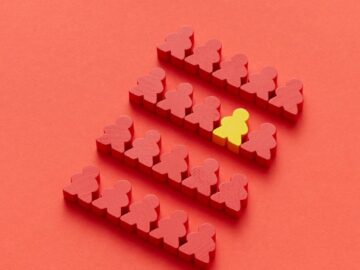 A group of red meeples with one yellow meeple standing out on a red background, symbolizing individuality.