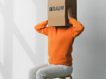 Crop anonymous person putting creased paper with Rubbish inscription in container with Brain title on head of female on chair