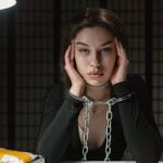 Woman in handcuffs, sitting in a dimly-lit room, appearing contemplative.