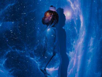 A woman stands against a galaxy projection with a serene profile, embodying cosmic dreams.