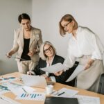 Three businesswomen discussing reports in a modern office environment.