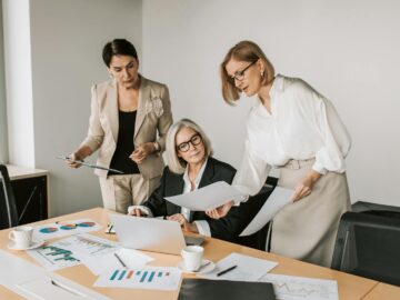 Three businesswomen discussing reports in a modern office environment.