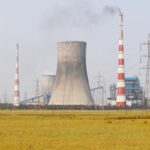 A cooling tower and smokestacks release emissions in a rural field near Vijayawada, India.