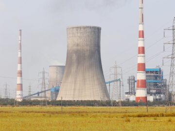 A cooling tower and smokestacks release emissions in a rural field near Vijayawada, India.