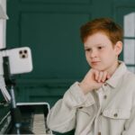 A focused young boy takes piano lessons online, showcasing the blend of education and music at home.