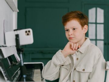 A focused young boy takes piano lessons online, showcasing the blend of education and music at home.
