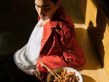 Fashionable male enjoying a bowl of noodles in a sunlit indoor restaurant setting.