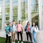 A diverse group of happy students standing outside a modern campus building.