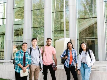 A diverse group of happy students standing outside a modern campus building.