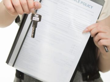 Close-up of person holding home insurance document and house key, symbolizing real estate and security.