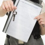 Close-up of person holding home insurance document and house key, symbolizing real estate and security.
