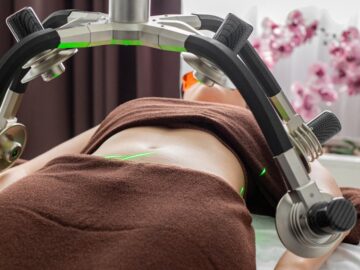 Crop anonymous female patient lying under lasers of fat loss machine on belly during treatment in light modern medical clinic