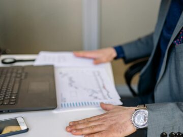 Businessman analyzing charts and graphs at his desk with a laptop and smartphone.