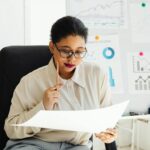 Businesswoman in glasses analyzing financial documents at her office desk.