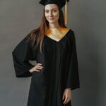 Confident young woman in graduation attire posing against a neutral background.