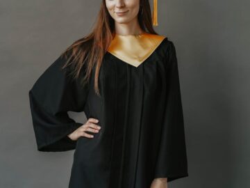 Confident young woman in graduation attire posing against a neutral background.