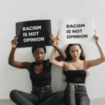 Two women holding signs with anti-racism message indoors.