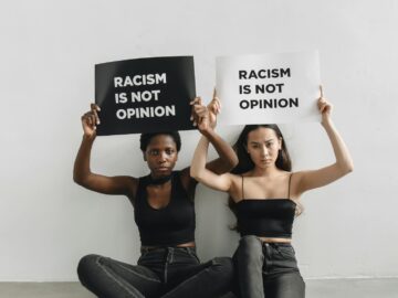 Two women holding signs with anti-racism message indoors.
