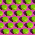 Delicious green macarons arranged in a vibrant repeating pattern on a pink surface.