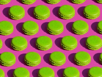 Delicious green macarons arranged in a vibrant repeating pattern on a pink surface.