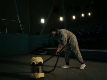 A cinema employee cleaning the theater floor with a vacuum cleaner under dim lights.