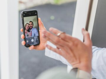 Close-up of hands holding a smartphone showing a couple taking a selfie outdoors.