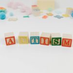 Wooden blocks spelling autism surrounded by colorful toys on a white background.