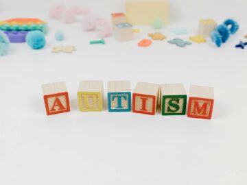 Wooden blocks spelling autism surrounded by colorful toys on a white background.