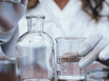 Chemist using a pipette and beakers for a laboratory experiment, wearing gloves.