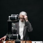 An elderly man competes in chess against a robotic arm, symbolizing strategy and technology fusion.