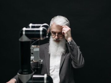 An elderly man competes in chess against a robotic arm, symbolizing strategy and technology fusion.