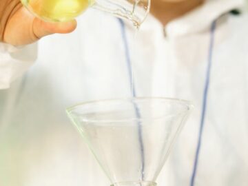 A scientist in protective gear pours a liquid into a flask, showcasing laboratory research.