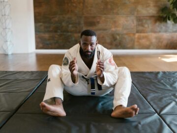 Martial artist wearing a gi sits on a mat, ready for training indoors.